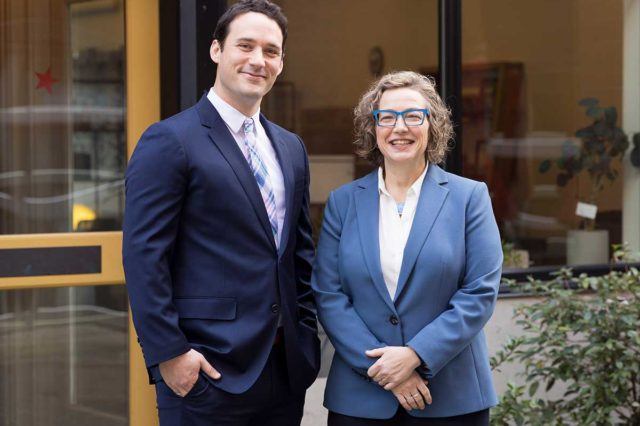 beth bloom and jay corker standing outside of office wearing blue suits